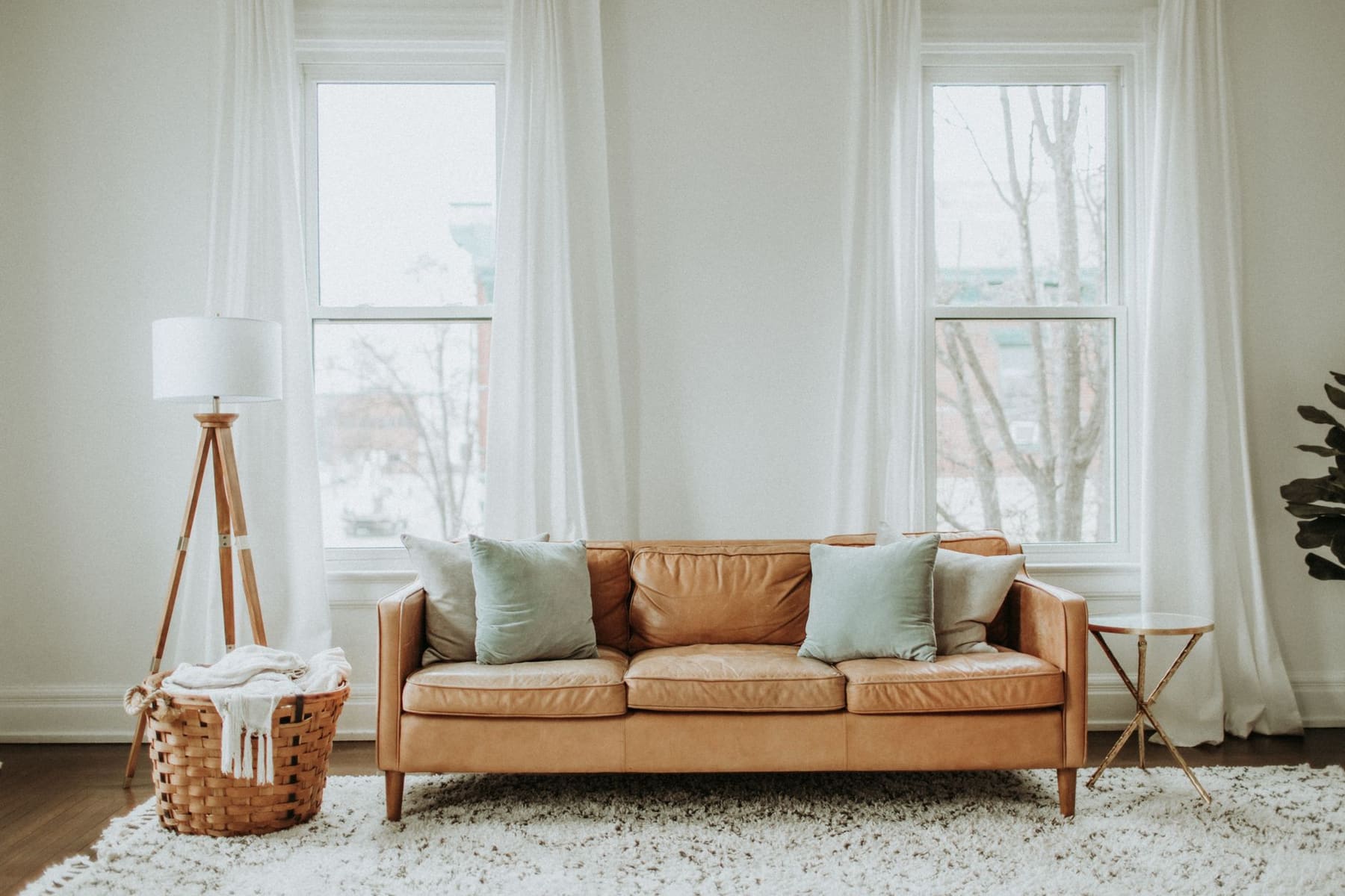 Bright living room with a tan leather sofa between two tall windows with sheer curtains