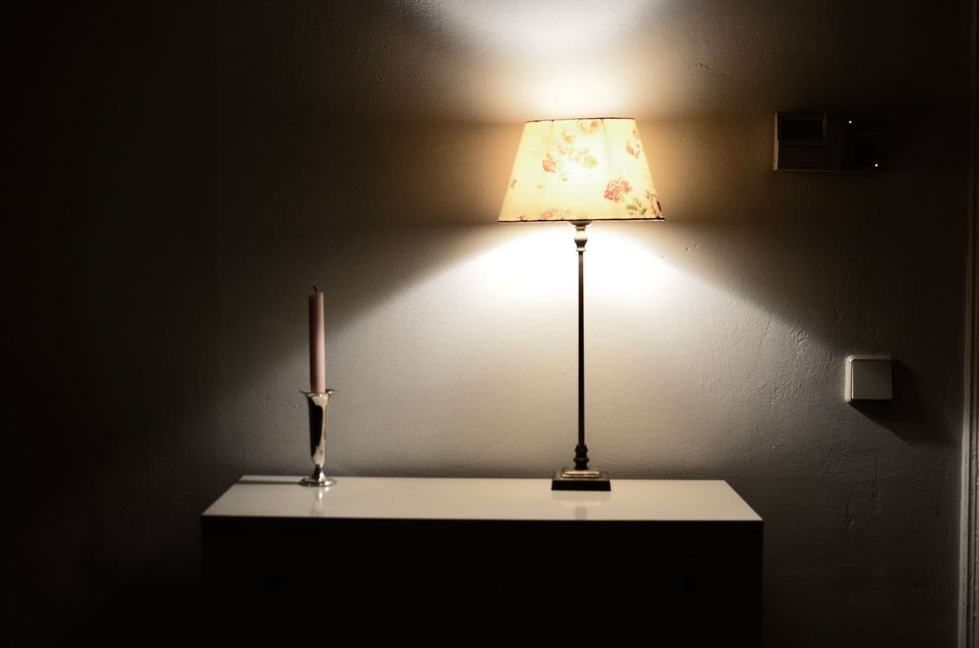Lit table lamp with a patterned shade on a white console in a dim room