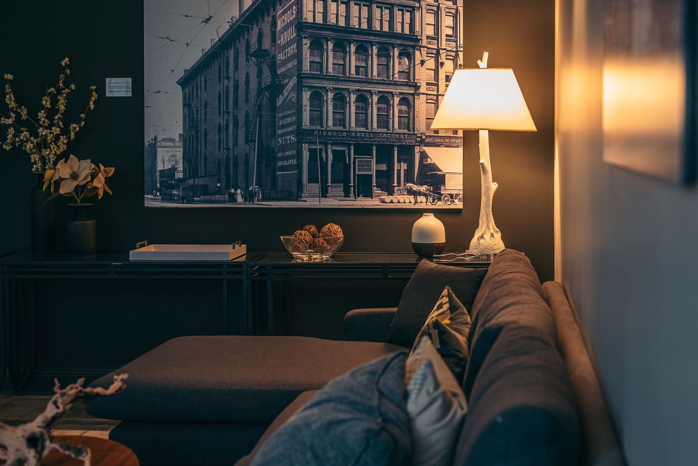 Living room corner with a lit lamp beside a sofa and framed wall art