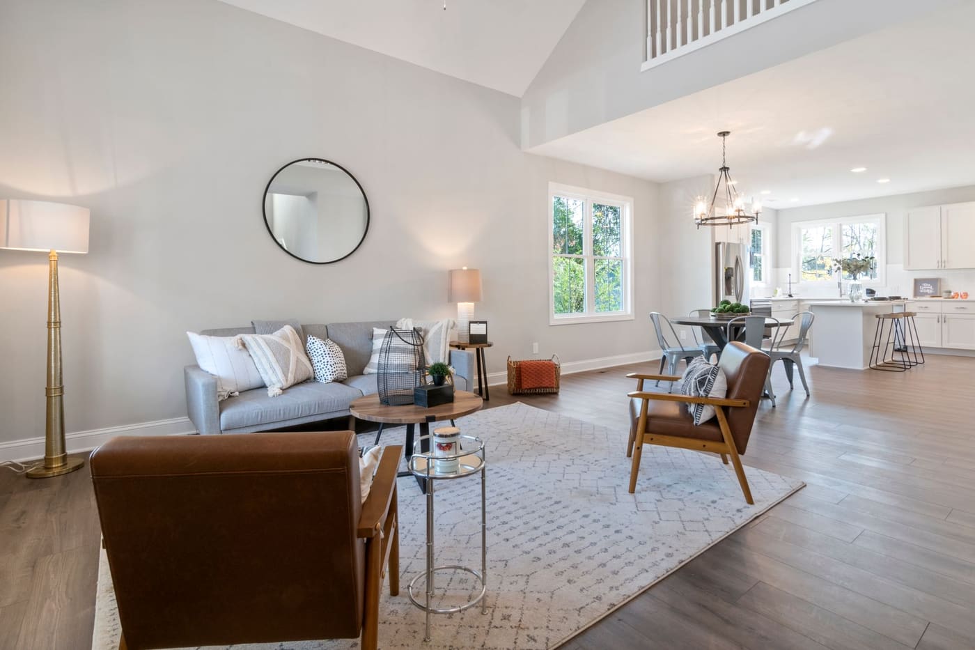 Light living room with a gray sofa, armchairs, a floor lamp and a round wall mirror