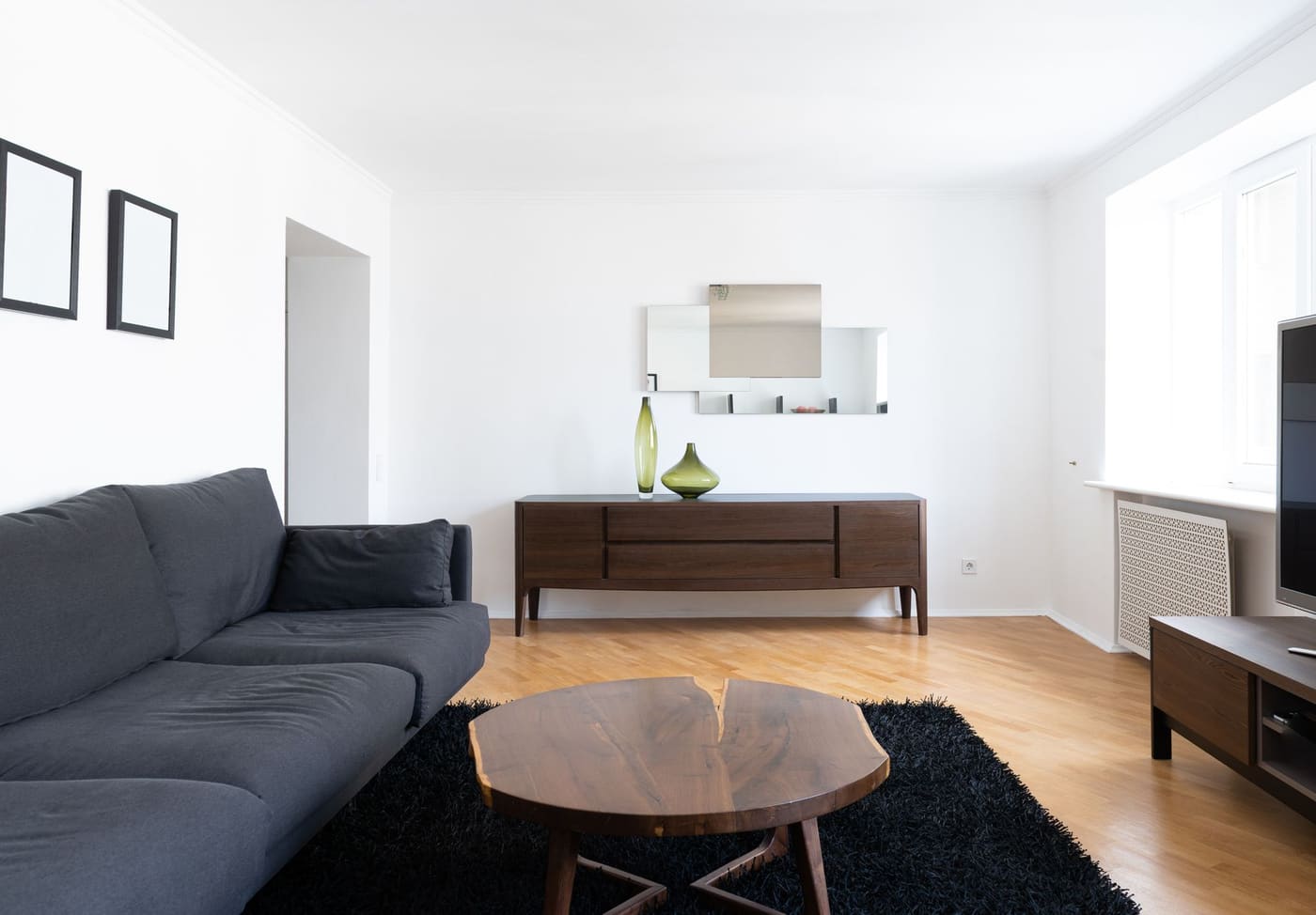 Living room with a gray sofa, a round wooden coffee table and a black rug