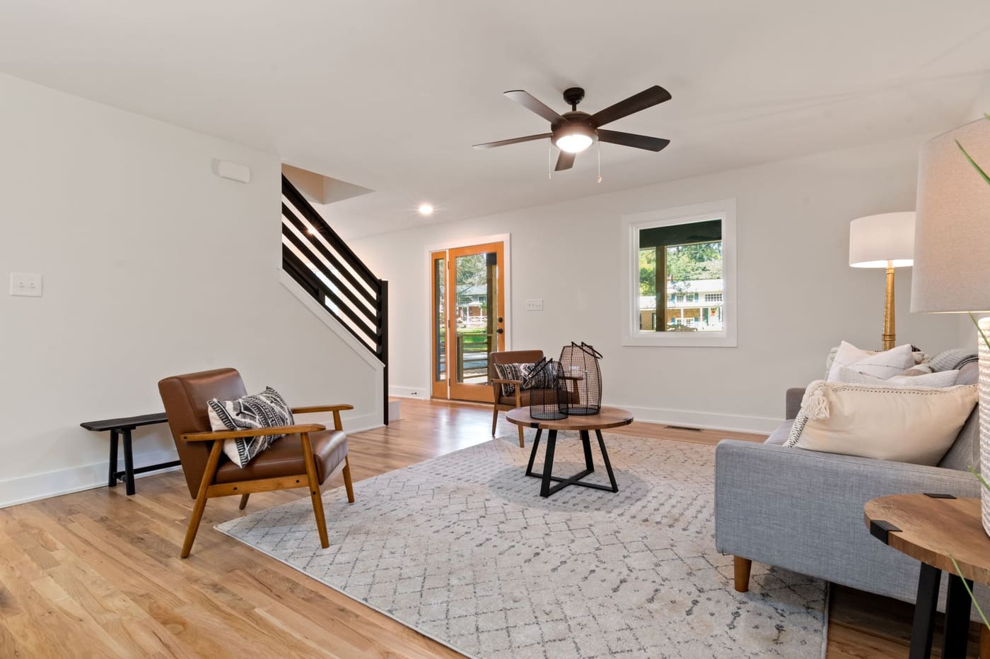 Living room with a wood floor, wooden armchairs, a patterned rug and a gray sofa