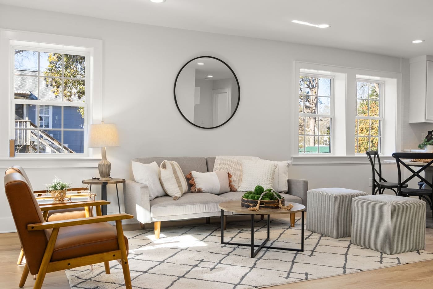 Bright living room with a gray sofa, an armchair, a round mirror and large windows