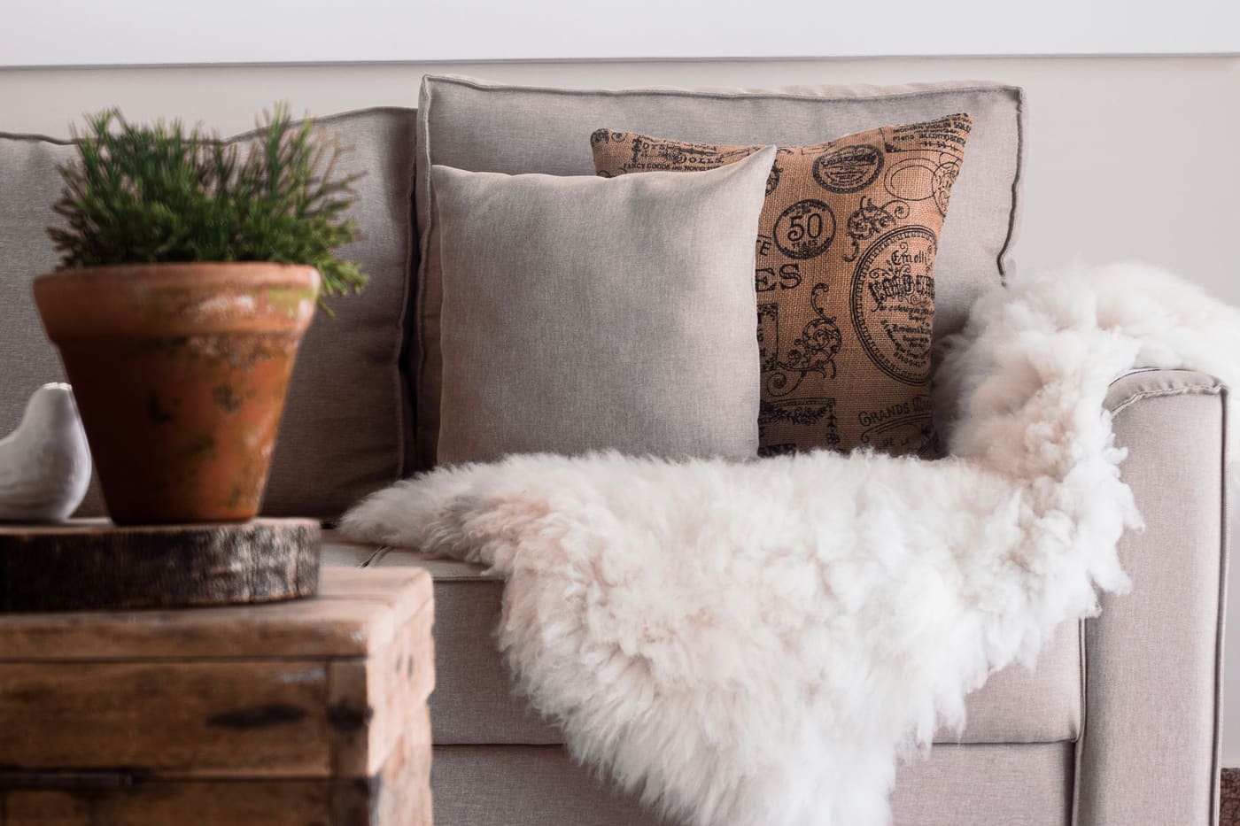 Sofa with cushions, a sheepskin throw and a terracotta plant pot on a wooden table