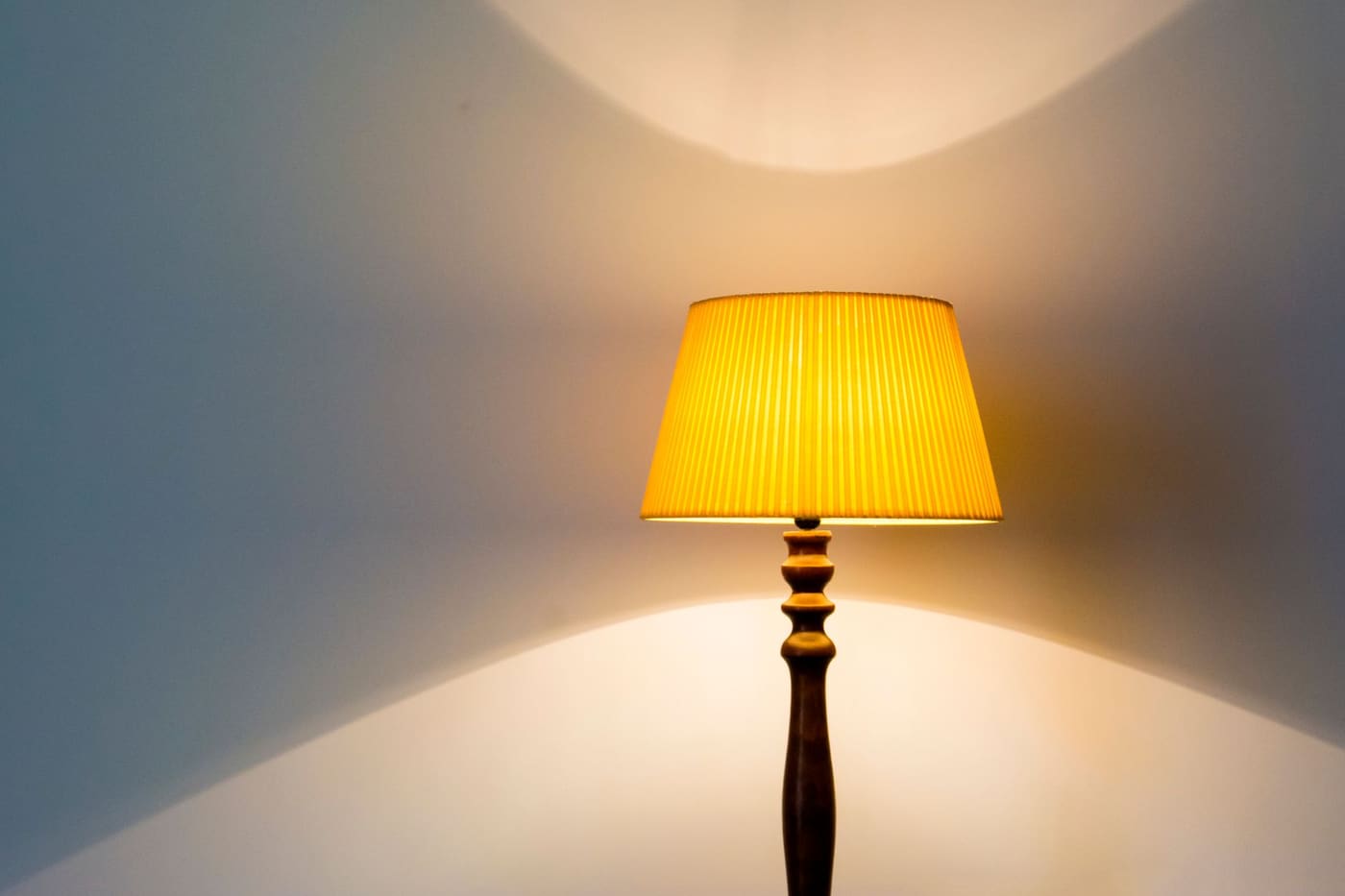 Floor lamp with a yellow pleated shade glowing against a white wall