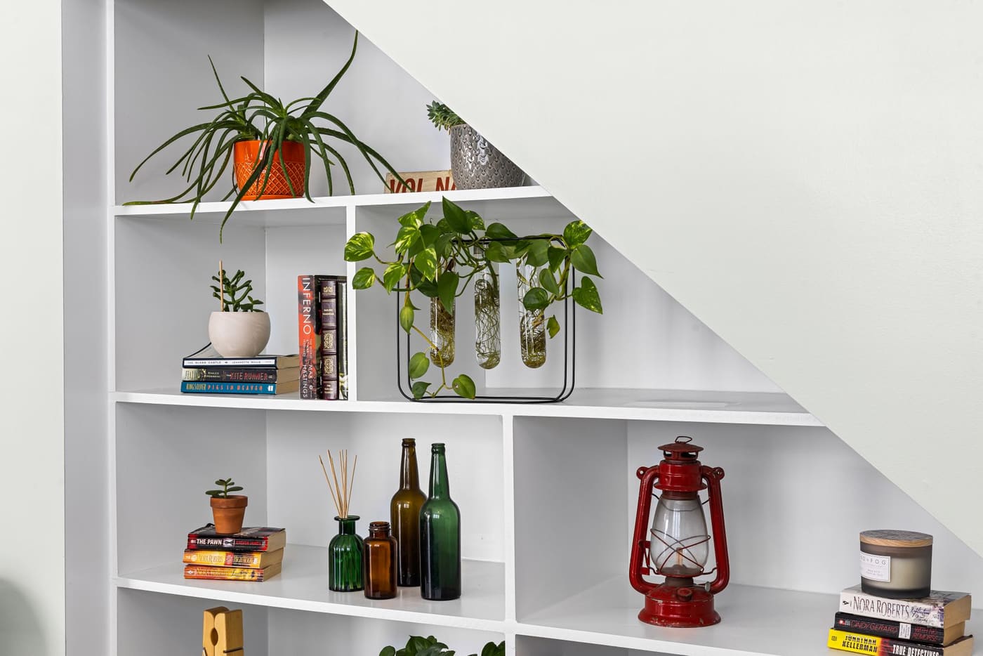 White shelves holding plants, books, bottles and a red lantern