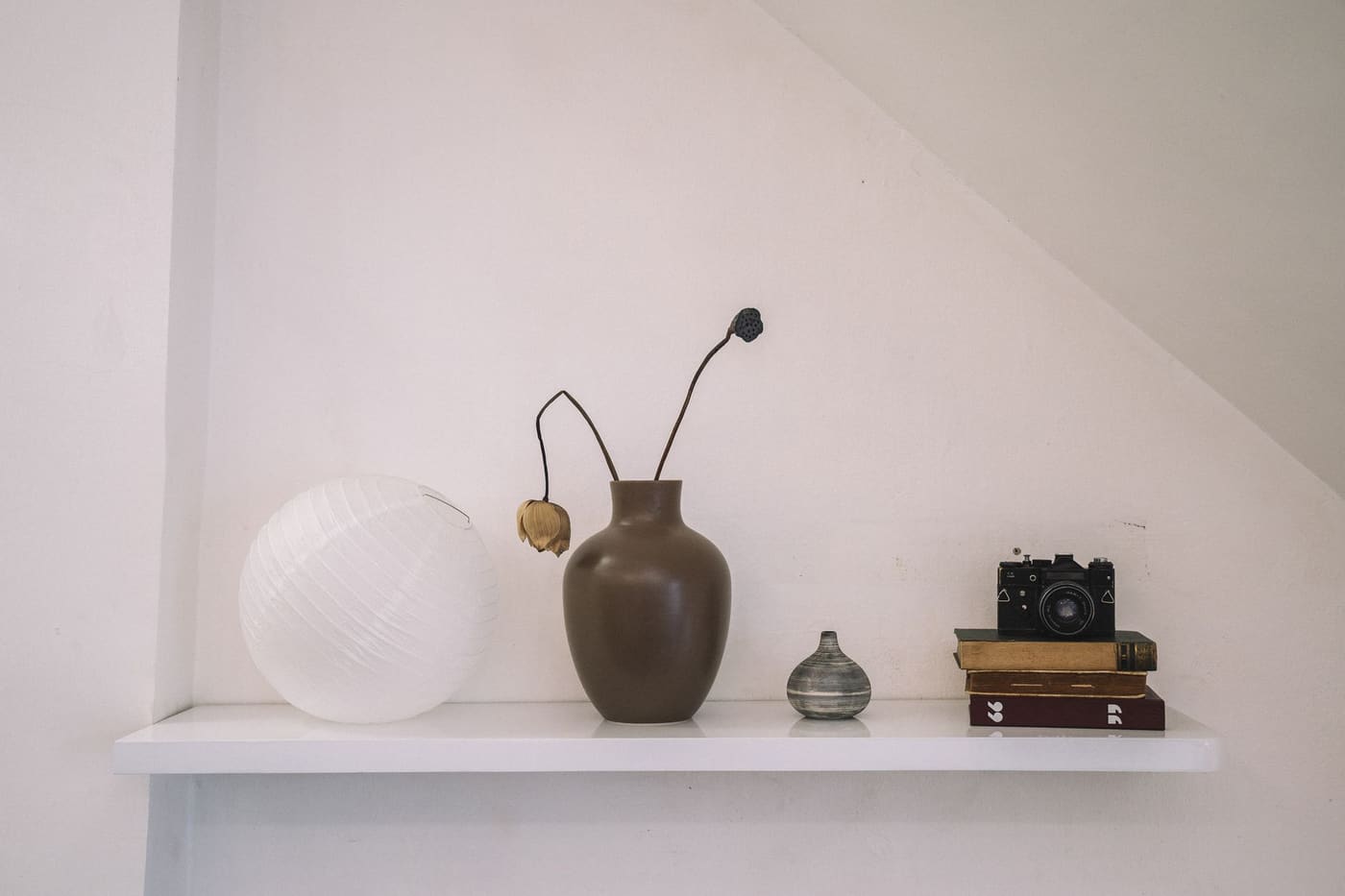 Floating white shelf with a vase of dried stems, a round white object and a few books
